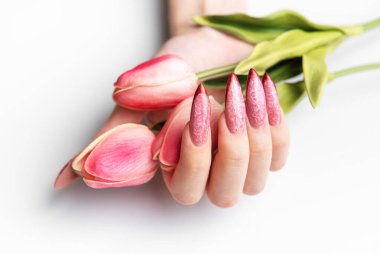 Pembe dizaynlı uzun topuklu tırnakları olan, narin pembe lale tomurcukları tutan bir kadın eli.