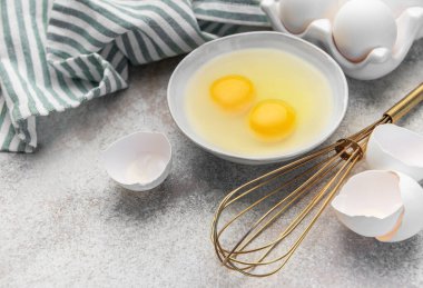 Bir kasede çiğ yumurta çırpılmış ve beton bir yüzey üzerinde kırılmış kabuklar.