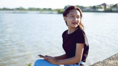 Genç Asyalı kız güzel gölü olan parkta oturuyor..