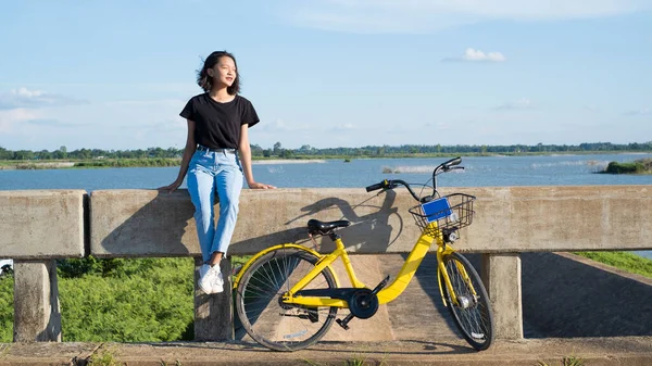 Młoda Dziewczyna Nosi Czarną Koszulę Dżinsy Siedzące Moście Żółtym Rowerem — Zdjęcie stockowe