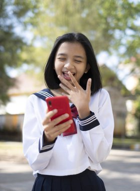 Güzel genç bir öğrenci okulda duran kırmızı akıllı telefonu tutuyor, okuldaki mutlu genç kız..