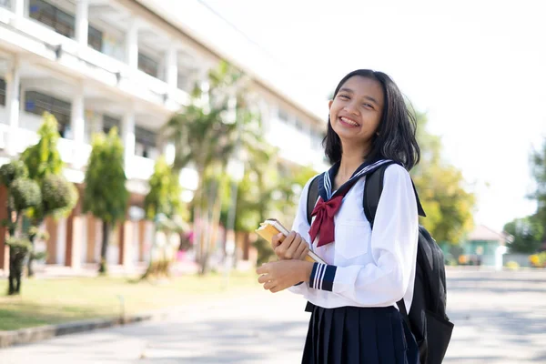 Sorridente Asiatica Giovane Ragazza Indossare Uniforme Tenere Libro Piedi Scuola — Foto Stock