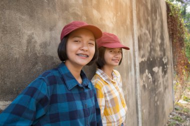 Mutlu iki Asyalı kız okulda eski duvar arkaplanlı kırmızı şapka takıyor..