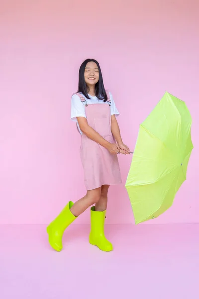 幸せな若いです女の子とともに緑傘緑色ブーツ上のピンクの背景 — ストック写真