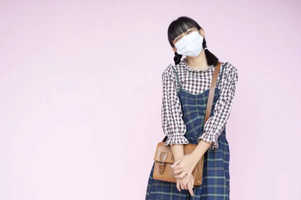 가방을 소녀는 배경에 마스크를 아시아 학생이며 반쪽인 아이입니다 — 스톡 사진