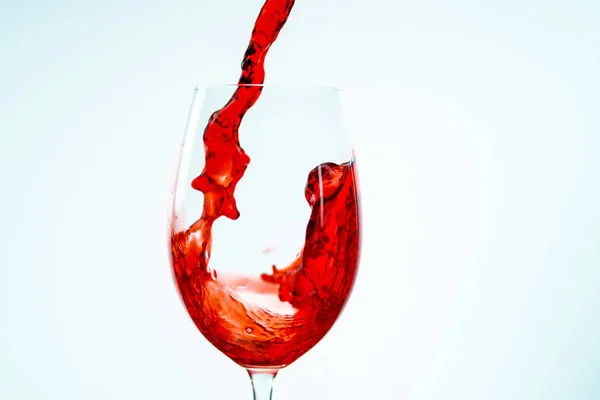 Een stroom rode wijn wordt op een witte achtergrond in een glas gegoten — Stockfoto
