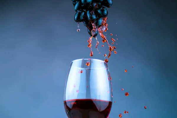 Kırmızı şarap kadehi mavi bulanık arka plana damlalar damlatarak yaklaşır.