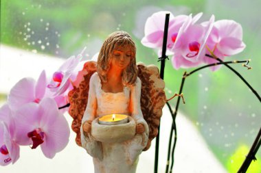 Arka planda çiçekli bir mum tutan bir meleğin heykeli.