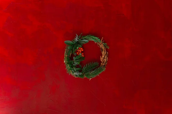 christmas wreath with fir and spruce branches and hawthorn on red wooden background top view photo