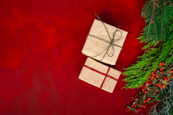 gift boxes covered with craft paper, with tree branches and hawthorn for christmas on red wooden background top view photo