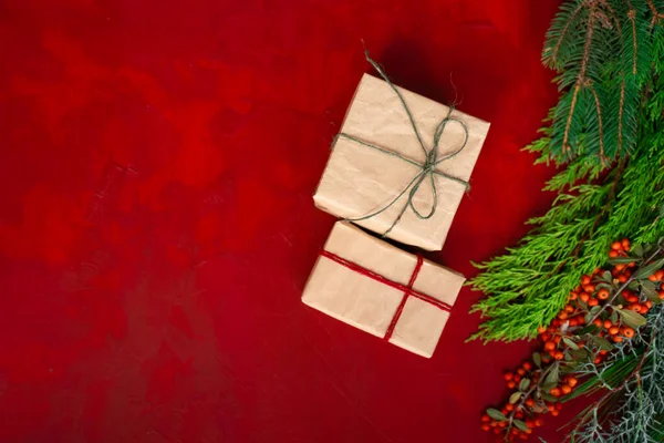 Hediye kutuları el işi kağıtları, ağaç dalları ve kırmızı ahşap arka planda Noel için dikenli fotoğraf.