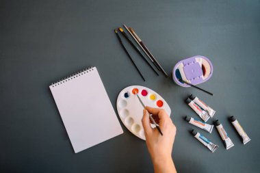 Evde kal. Tecrit ya da karantina. Suluboya resim yapan genç bir kız. Pencerenin önünde oturuyor. Genç hobileri. Parlak renkli boya ve fırçayla suluboya paleti