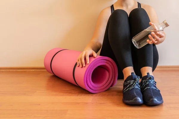 Kadın spordan sonra dinleniyor. Pembe mat su şişesi. Egzersiz yaptıktan sonra elinde şişe tutarak su içmek. Çevrimiçi yoga meditasyon antrenmanı. Karantina koronavirüsü kilitlendi. Aktif ol. sağlıklı yaşam.