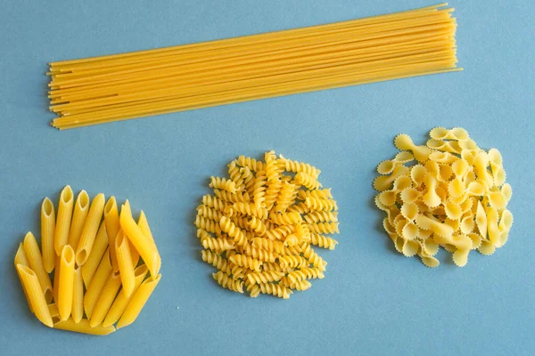 Penne, farfalle tonde kelebeği, kepçe, açık mavi desenli arka planda spagetti. Soyut, makarna. Üst görüntü fotoğrafı. düzenli.