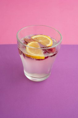 Bir bardak köpüklü su kokteyli dilimlenmiş limon, kiraz ve böğürtlen. Alkolsüz içecek, içecek. mor desenli arka plan ve pembe arkaplan. Karbonatlı su ve baloncuk. Soyut, kapat.