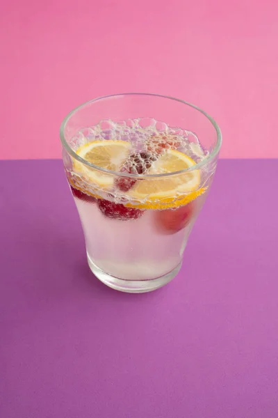 Bir bardak köpüklü su kokteyli dilimlenmiş limon, kiraz ve böğürtlen. Alkolsüz içecek, içecek. mor desenli arka plan ve pembe arkaplan. Karbonatlı su ve baloncuk. Soyut, kapat.