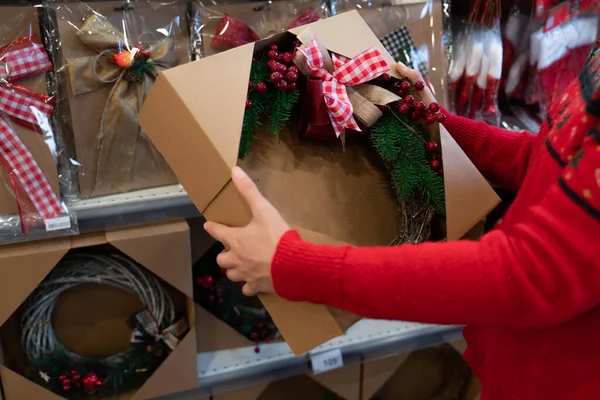Noel için markette alışveriş yapan kadın, yeni yıl süsü. Yılbaşı çelengi, kasap süpürgesi, kurdele, arkadaşlar ve aile için şube hediyesi. çirkin Noel süveteri. Koronavirüs zaman salgını.