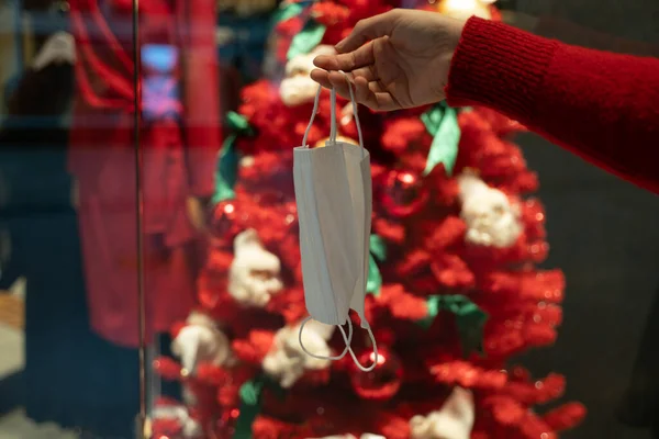 Süslü Noel ağacının önünde tıbbi maske tutuyor. yeni normal. Koronavirüs salgını. 2021 Noel ve Yeni Yıl.