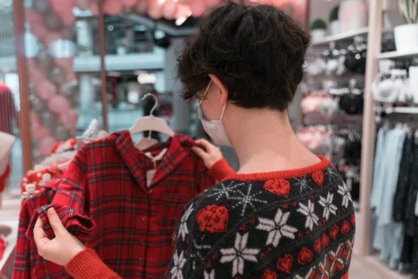 Tıbbi maske takan bir alışveriş kadını. Noel ve yeni yıl alışverişi. hediye fikirleri. çirkin Noel süveteri. 2021