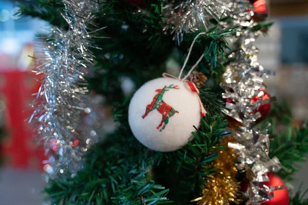 Süslü bir Noel ağacında asılı duran beyaz top. Yeşil, kırmızı, gümüş, altın, geyik, Noel ve yeni yıl ağacı süslemesi. Bokeh ışığı. Spruce, kapat. 2021