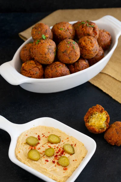 Traditional Middle Eastern food, Falafel (tamiya) with hummus and pickles on black wooden background and yellow table cloth. Selective focus some areas are blurred.