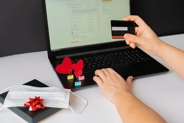 Sevgililer Günü milenyumu boyunca internetten laptop, kredi kartı ve tıbbi maske kullanarak alışveriş yapmak. Hediye siparişi Coronavirus konsepti kilitleme 2021 İnternet bankacılığı, ödeme, sürpriz