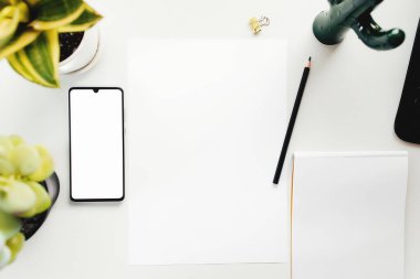 Beyaz masada akıllı telefon, evden çalışma, ofis eşyaları.