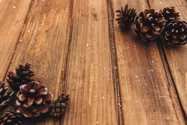 Cones and snow on brown wooden background