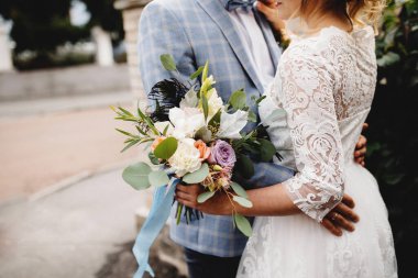 Beyaz elbiseli gelin elinde düğün buketi tutuyor. Damat gelini kucaklıyor.