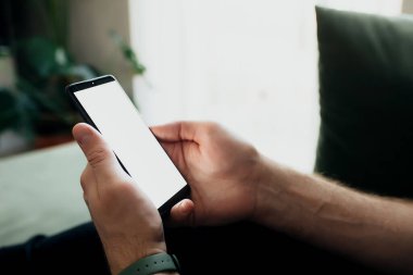 Adam elinde beyaz ekranlı akıllı telefon tutuyor.
