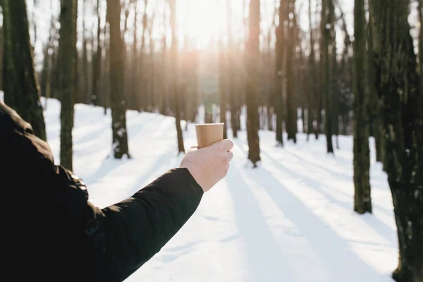 Le gars tient une tasse de café en papier dans sa main dans la forêt enneigée — Photo