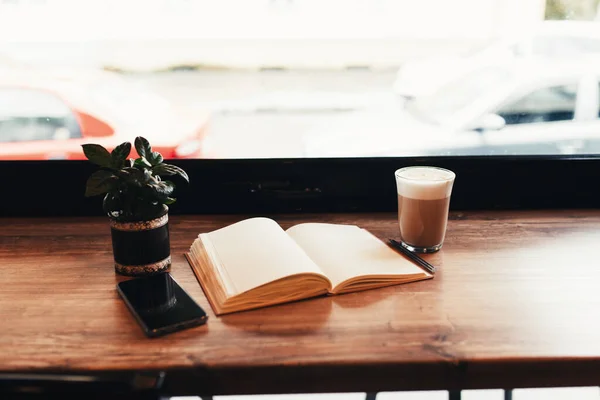 Secangkir kopi, notebook, telepon di meja di kafe. Latar belakang kabur — Stok Foto