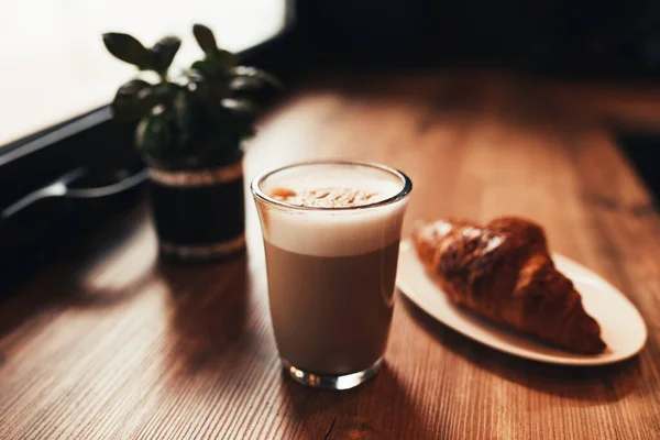 Чашка кофе, круассан за столом у окна в кафе. Размытый фон — стоковое фото