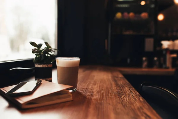 Secangkir kopi, notebook, telepon di meja di kafe. Latar belakang kabur — Stok Foto