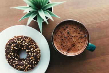 Beyaz tabakta çörekler, ahşap masada kahve ve yeşil bitki.