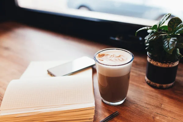 Secangkir kopi, notebook, telepon di meja di kafe. Latar belakang kabur — Stok Foto