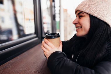 Gülümseyen bir kız, kafe yakınlarında elinde bir fincan kağıt kahve tutuyor. Arka plan bulanık. Yüksek kalite fotoğraf