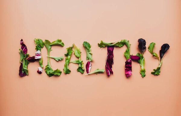 Text healthy using green and purple salad leafs mix on beige background. High quality photo