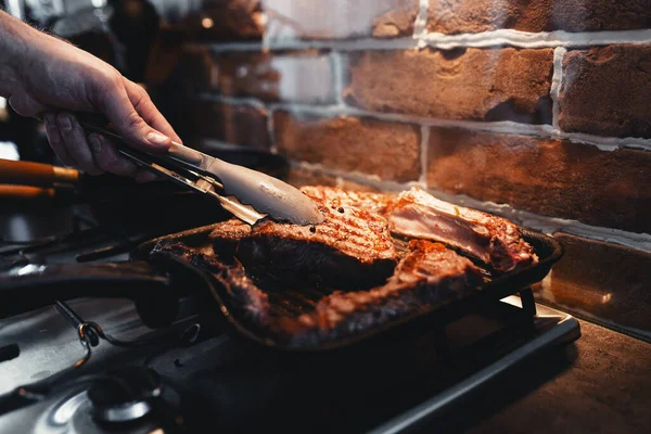 Izgara tavasında baharatlı biftek pişirirken eli maşayla bifteğe dönüyor. Yüksek kalite fotoğraf