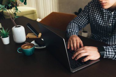 Laptopta çalışan bir adam bir fincan kahve, çikolatalı kek, telefon, bitki. Yüksek kalite fotoğraf