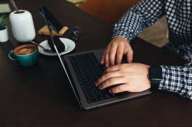 Laptopta çalışan bir adam bir fincan kahve, çikolatalı kek, telefon, bitki. Yüksek kalite fotoğraf