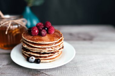 Beyaz tabakta böğürtlen ve bal ile sulu krepler, kaşık, kavanoz, ahşap masa. Yüksek kalite fotoğraf