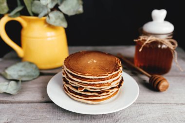 Beyaz tabakta ballı krep, kaşık, kavanoz, ahşap masa, okaliptüslü sarı vazo. Yüksek kalite fotoğraf