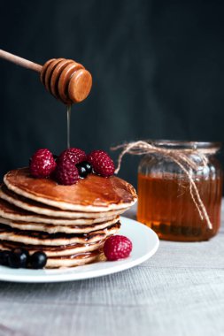 Beyaz tabakta böğürtlen ve bal ile sulu krepler, kaşık, kavanoz, ahşap masa. Yüksek kalite fotoğraf