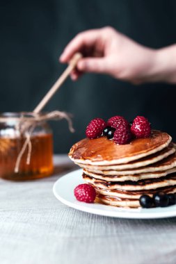 Böğürtlenli krep ve beyaz tabakta bal, kavanozda kaşık, ahşap masa. Yüksek kalite fotoğraf