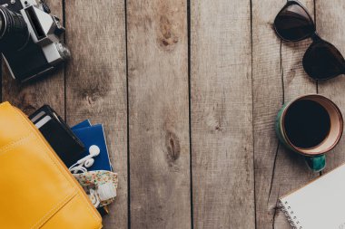 Pasaportlar, siyah cüzdan, el çantası, koruyucu maske ve dezenfektan, not defteri ve kulaklık, gözlük, kahve fincanı, tahta arka planda fotoğraf makinesi. Yüksek kalite fotoğraf