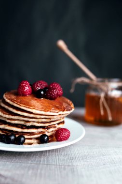 Beyaz tabakta böğürtlen ve bal ile sulu krepler, kaşık, kavanoz, ahşap masa. Yüksek kalite fotoğraf