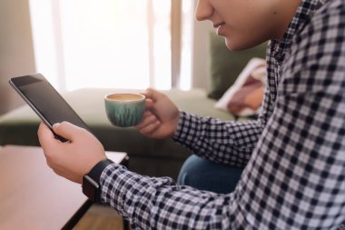 Gülümseyen adam elinde tutuyor ve siyah ekran ve kahve fincanıyla akıllı telefon okuyor. Arka plan bulanık. Yüksek kalite fotoğraf