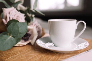Romantik bir sabah. Yatağında çiçekler olan ahşap sehpa, kahve fincanı, çiçekler, not defteri, kalem. Okaliptüs ve şakayıklı leylak gülleri. Yüksek kalite fotoğraf