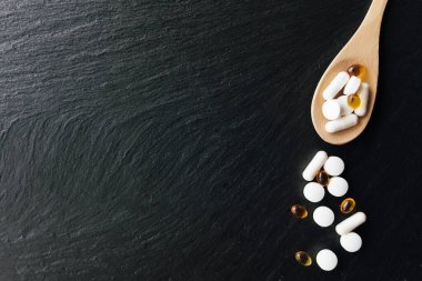 Omega 3 ve vitamin kapsülleri tahta kaşıkta siyah beton arka planda yatıyordu. Sağlık konsepti. Vitamin hapları. Yüksek kalite fotoğraf
